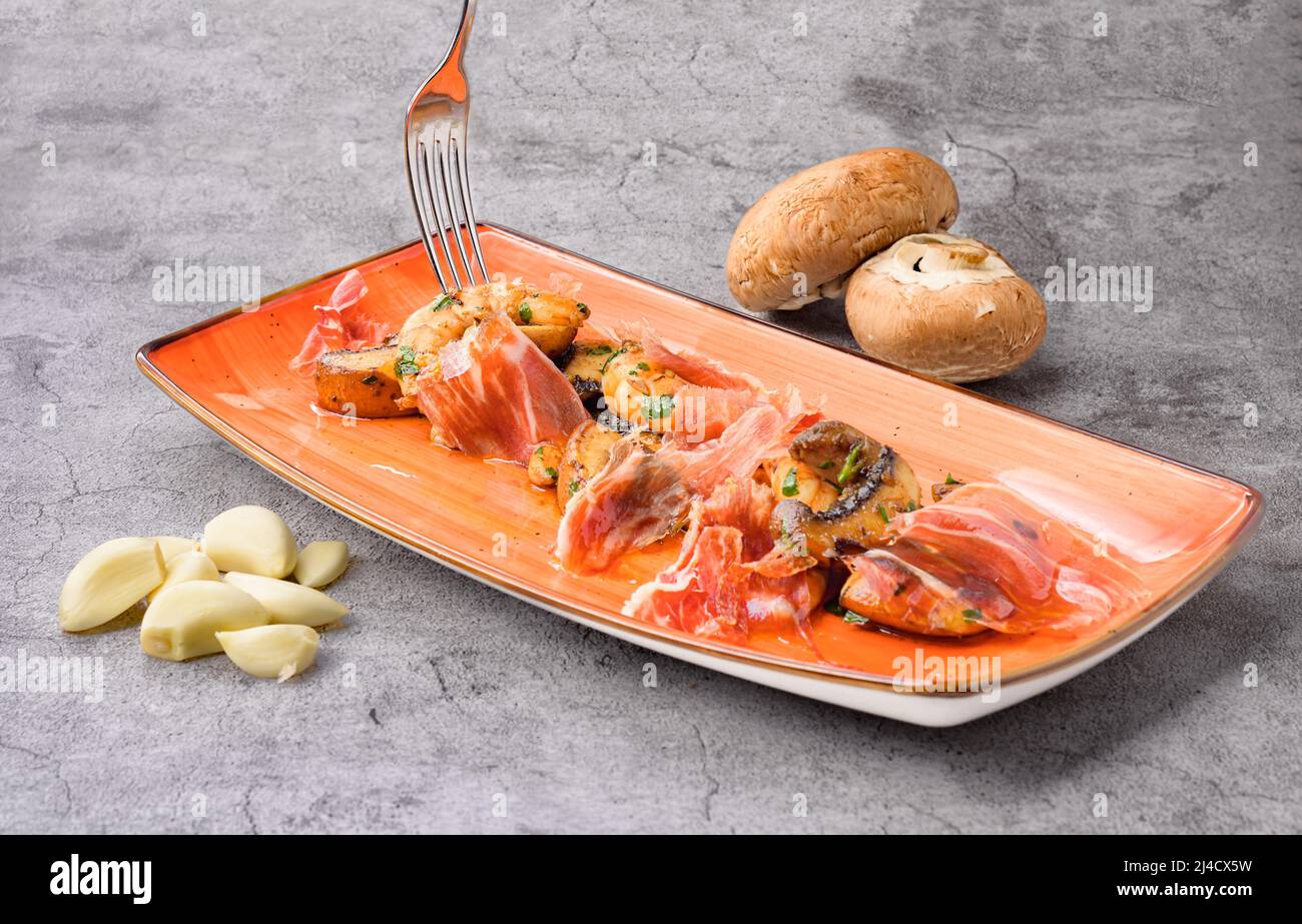 Köstliche Mahlzeit mit Scheiben serrano-Schinken, Pilzen und Garnelen auf dem Teller Stockfoto