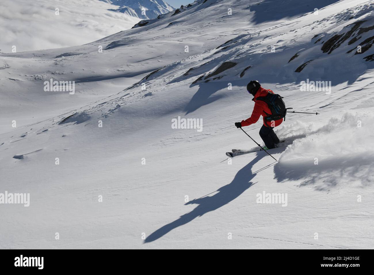 Skifahrer, die einen pudrigen Berghang hinunterfahren Stockfoto