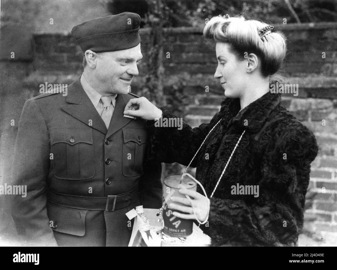 JAMES CAGNEY in London, um während des Zweiten Weltkriegs US-Truppen in England zu unterhalten, kauft eine Flagge von Miss MARION CONDY für den Tag der Roten Armee am 23. 1944. Februar Stockfoto