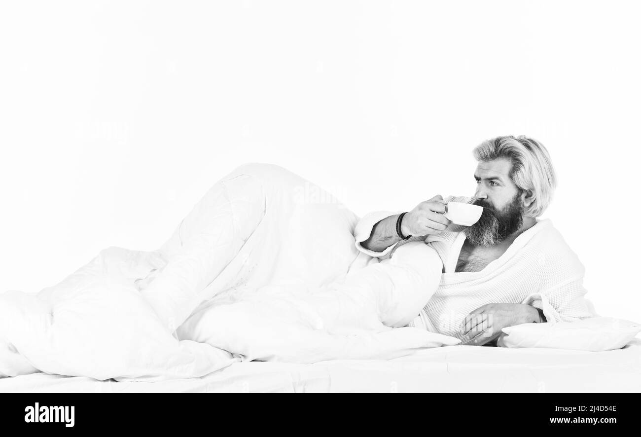 Genießen Sie den morgendlichen Kaffee. Der Körper wurde der wesentlichen Komponente für eine gute Gesundheit und Energie beraubt. Schöner Mann trinkt Kaffee. Reifer bärtiger Mann im Bett Stockfoto