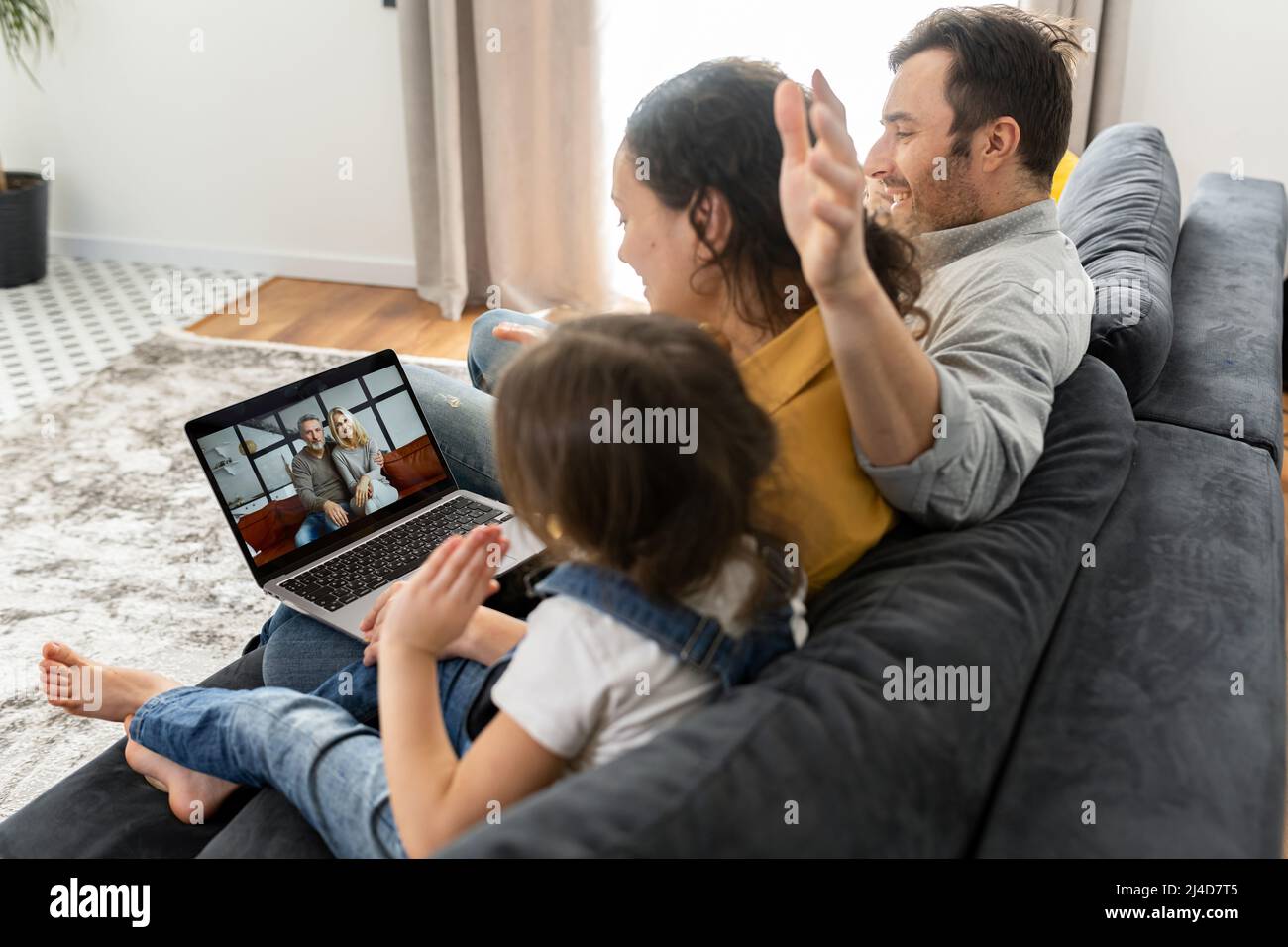 Vierköpfige Familie mit Laptop für Videoverbindung mit Großeltern oder Familie. Multirassische Mutter, Vater und zwei Kinder winken in der Webcam des Laptops, Videoanruf, virtuelles Konferenzkonzept Stockfoto