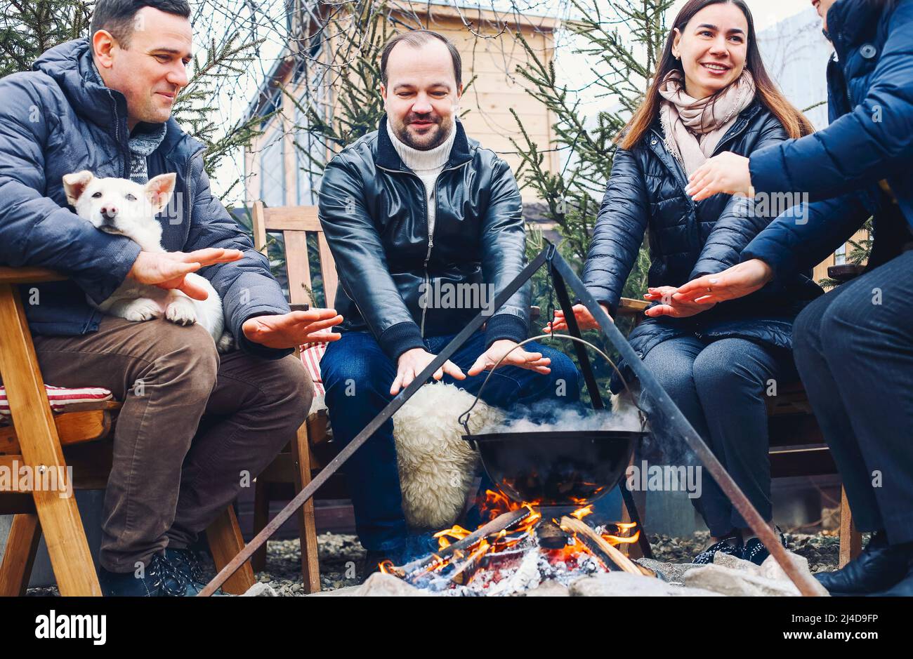 Traditioneller Glühwein mit Orangenscheiben, der im Winter auf dem Land über brennenden Holzstämmen im Topf bereitet, Freunde am Wintertag Stockfoto