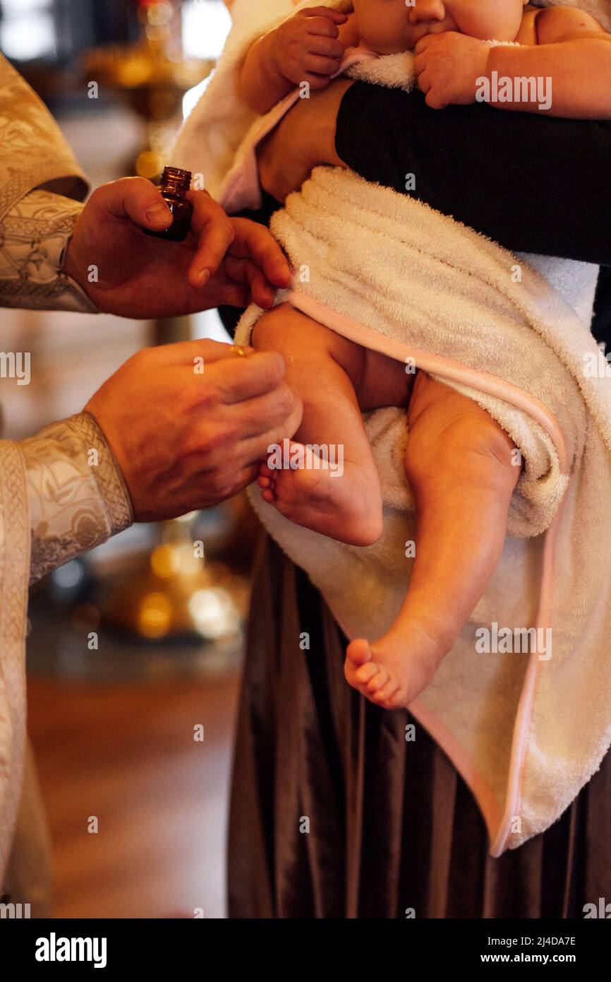 Zugeschnittenes Foto des Priesters in Soutane, der während der Zeremonie der Taufe heiliges Öl für die Salbung der Füße des Babys im Handtuch hält. Stockfoto