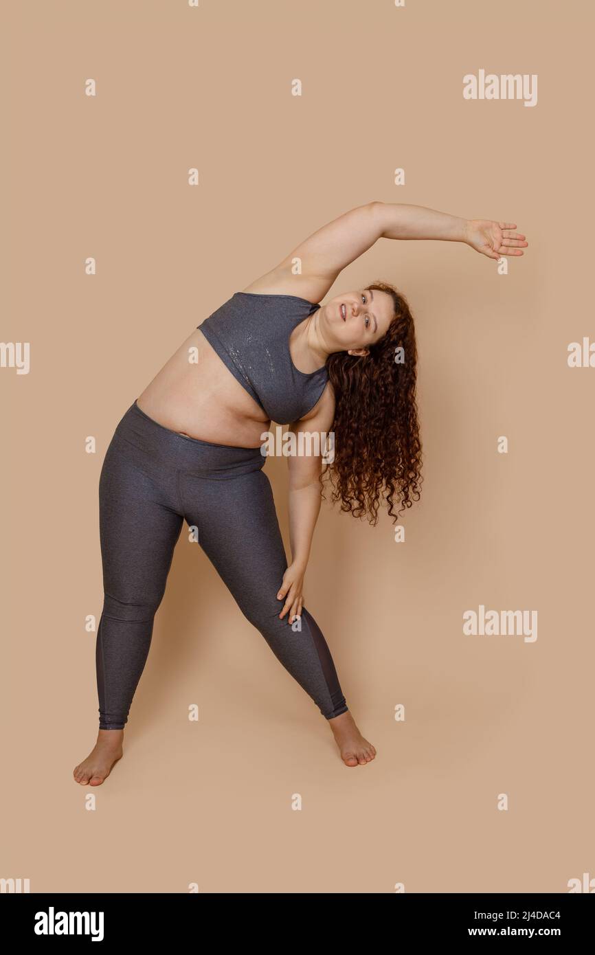 Konzentriere dich auf rothaarige übergewichtige Frau, die Sportturnen macht, schiebe die Arme nach rechts. Körper positiv, Gewichtsverlust Stockfoto