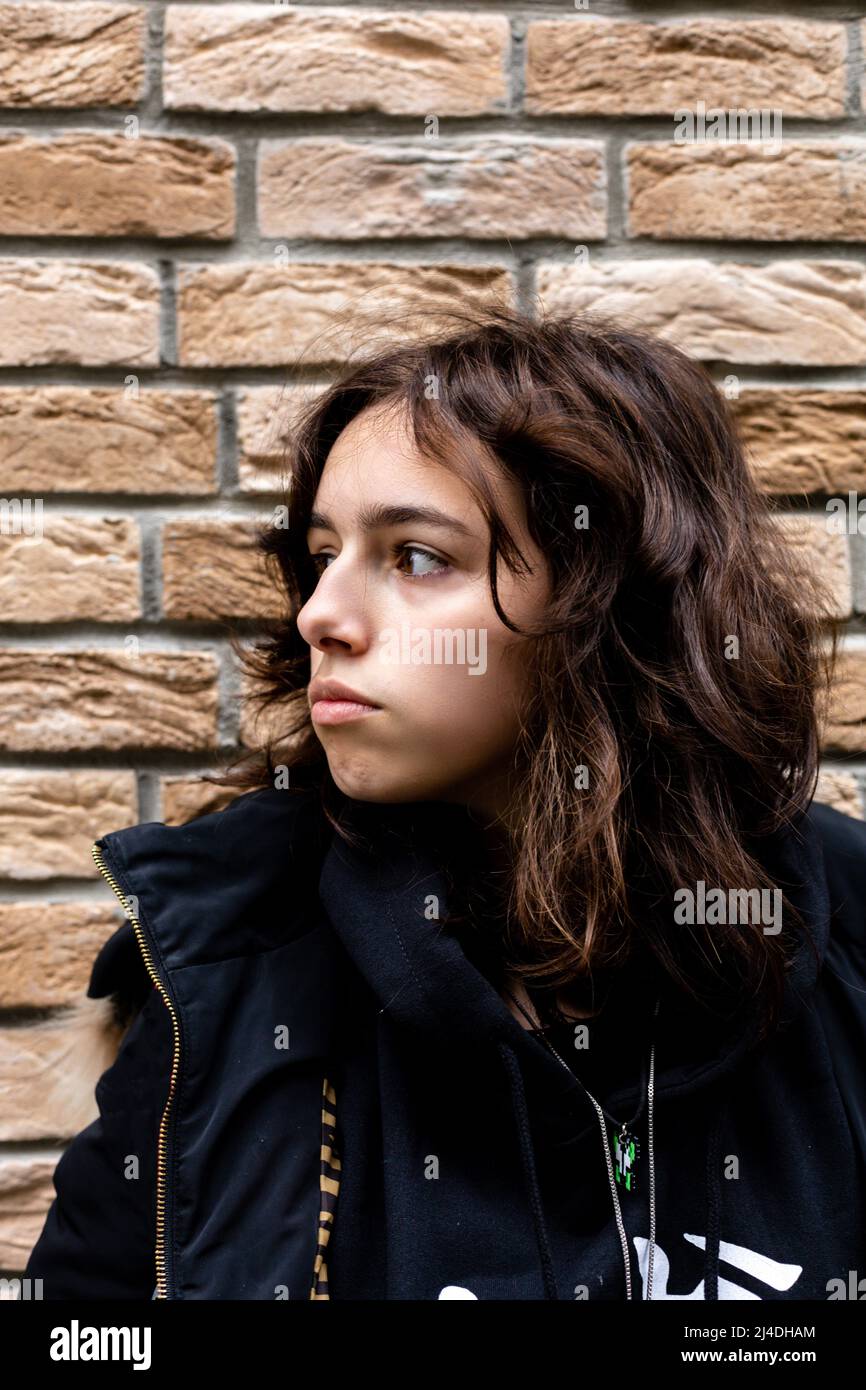 Porträt eines Teenagers vor einer Ziegelwand. Schwarz trägt Teenager, der zur Seite schaut Stockfoto