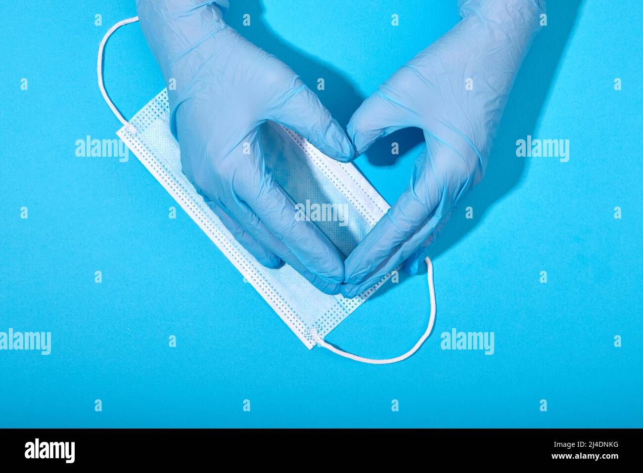 Hände in Latexhandschuhen machen Zeichen in Form von Herz auf dem Hintergrund der blauen medizinischen Maske close-up Stockfoto