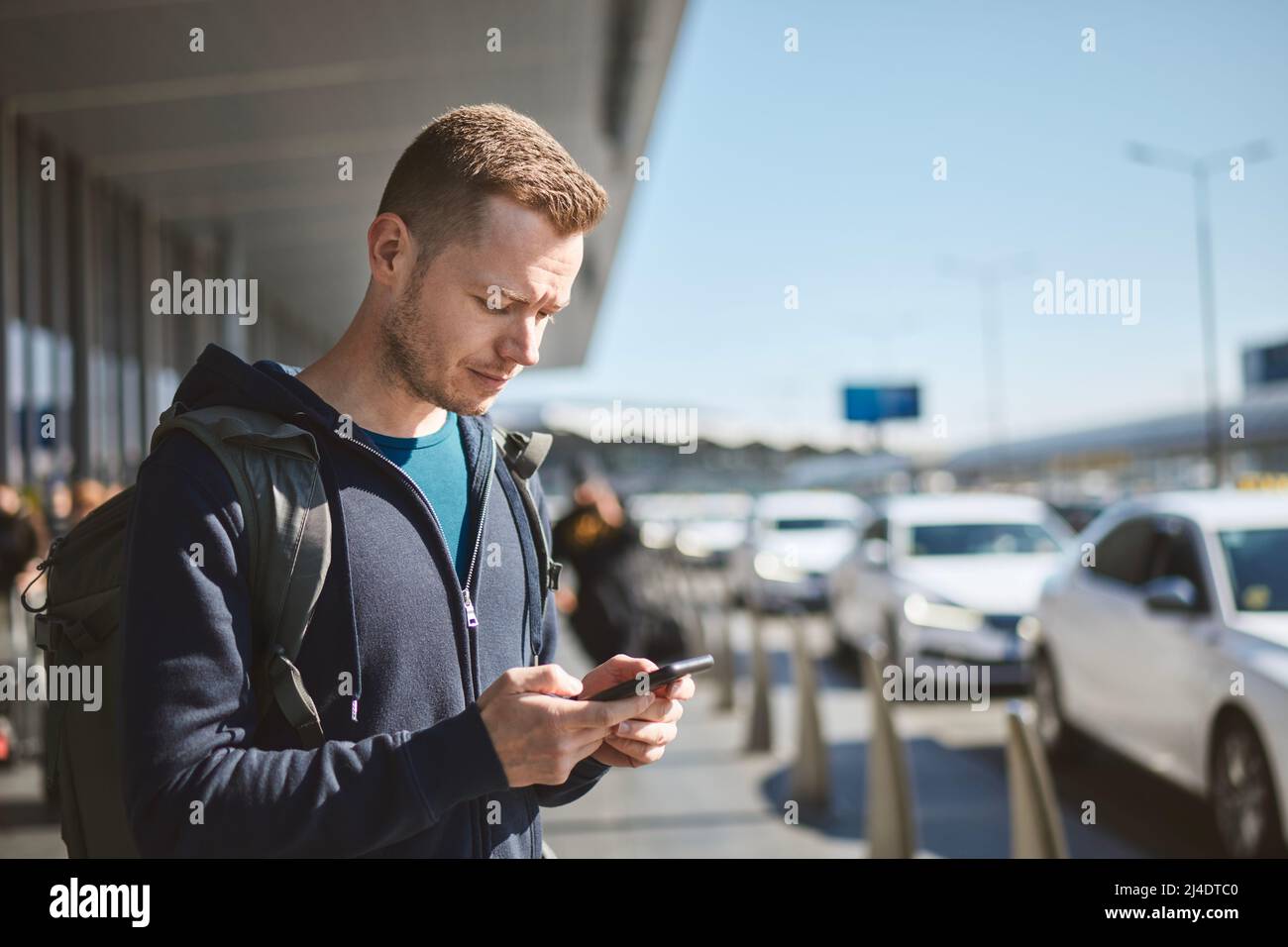 Mann hält Smartphone und benutzt mobile App gegen eine Reihe von Taxiwagen. Themen Moderne Technologie, Carsharing und Reisen. Stockfoto