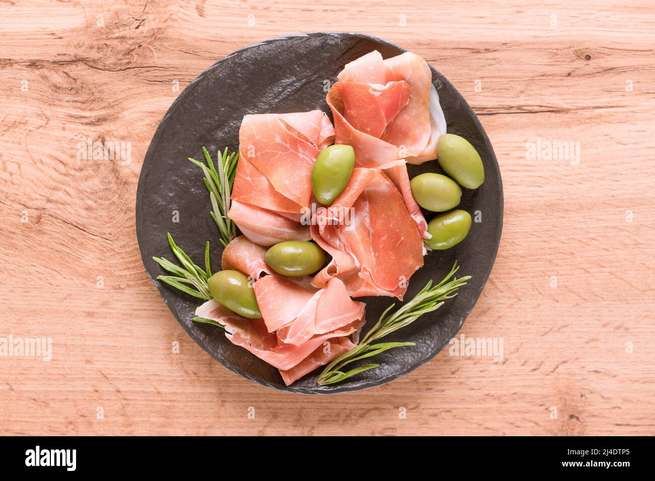 Charcuterie-Tafel mit Proscuitto, serviert mit Oliven auf Holztisch. Schwarzer Teller mit traditionellen italienischen Antipasti. Selektiver Fokus Stockfoto