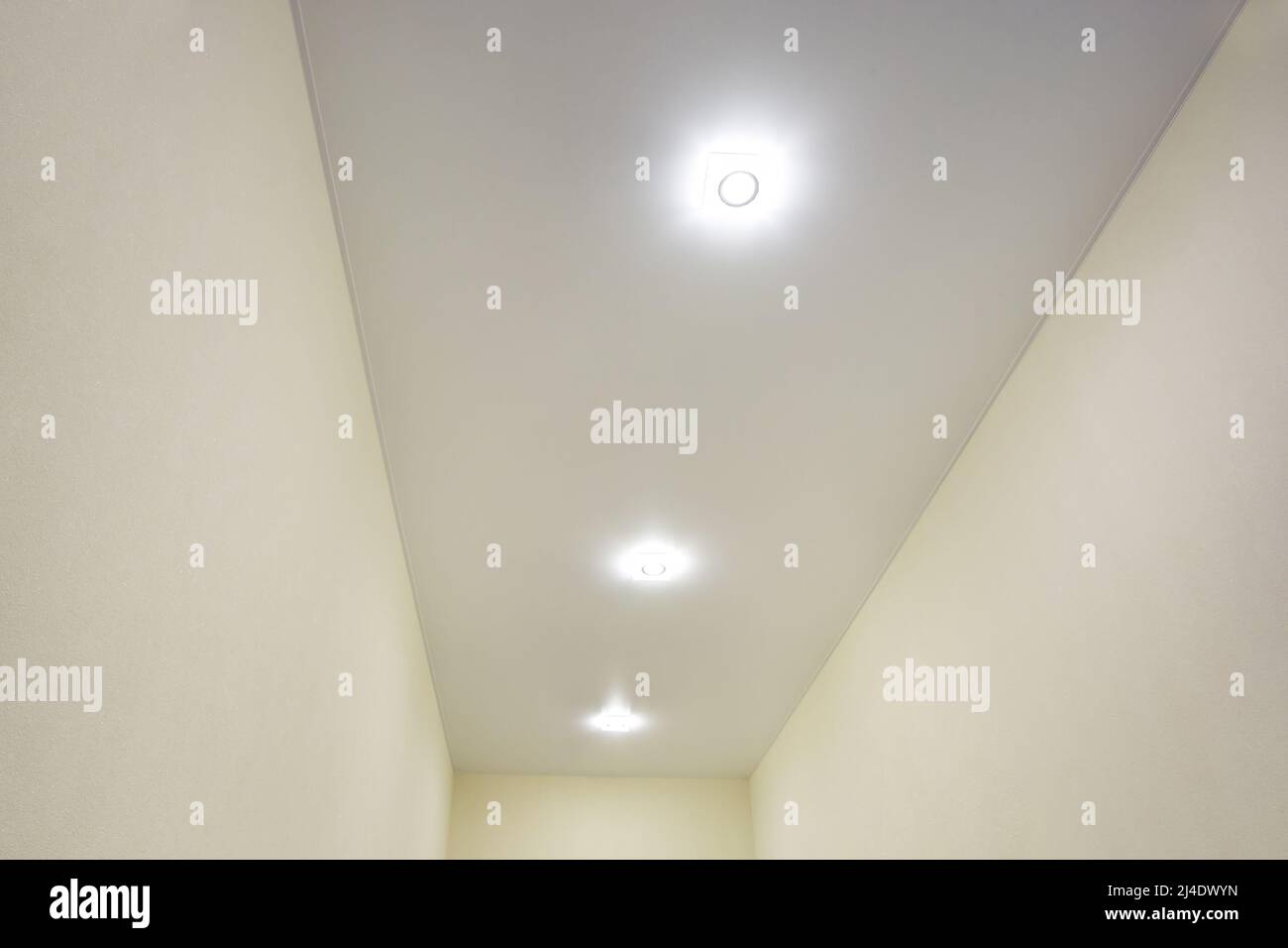 Abgehängte Decke mit Halogenstrahlern und Trockenmauerkonstruktion im leeren Raum in Wohnung oder Haus. Stretchdecke weiß und komplex. Stockfoto