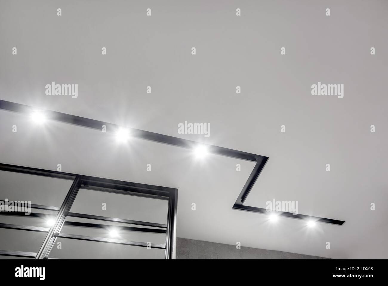 Abgehängte Decke mit Halogenstrahlern und Trockenmauerkonstruktion im leeren Raum in Wohnung oder Haus. Stretchdecke weiß und komplex. Stockfoto