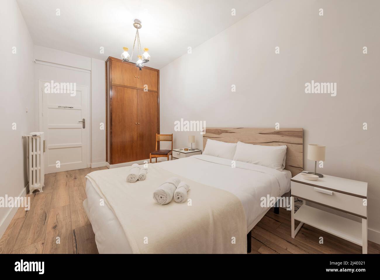Schlafzimmer mit Doppelbett mit Rollhandtüchern und Einbauschrank mit Holztüren und einteiligem Kofferraum, einteiligem Kopfteil aus Holz und zwei weißen Einzelbetten Stockfoto