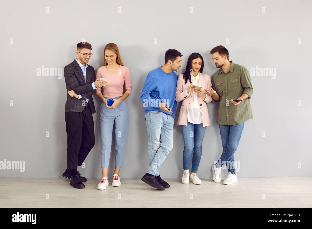 Eine Gruppe junger Männer und Frauen, die im Büro stehen und ihre Mobiltelefone gemeinsam nutzen Stockfoto