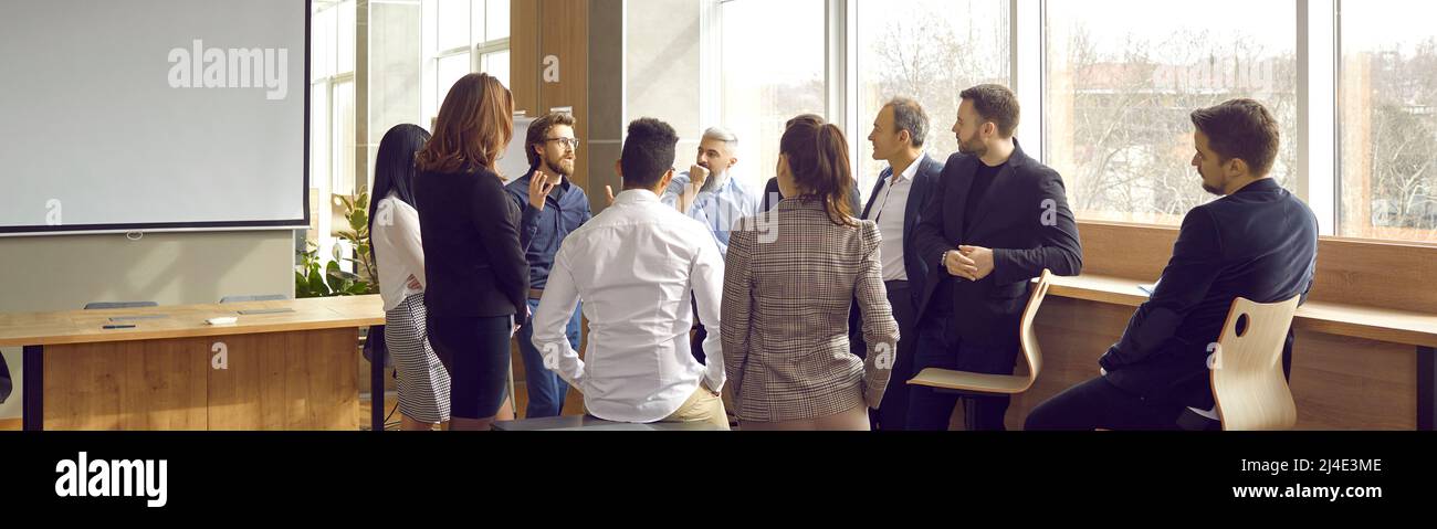 Kreativer Business-Lehrer im Gespräch mit einer Gruppe von Mitarbeitern während der Besprechung im Büro Stockfoto