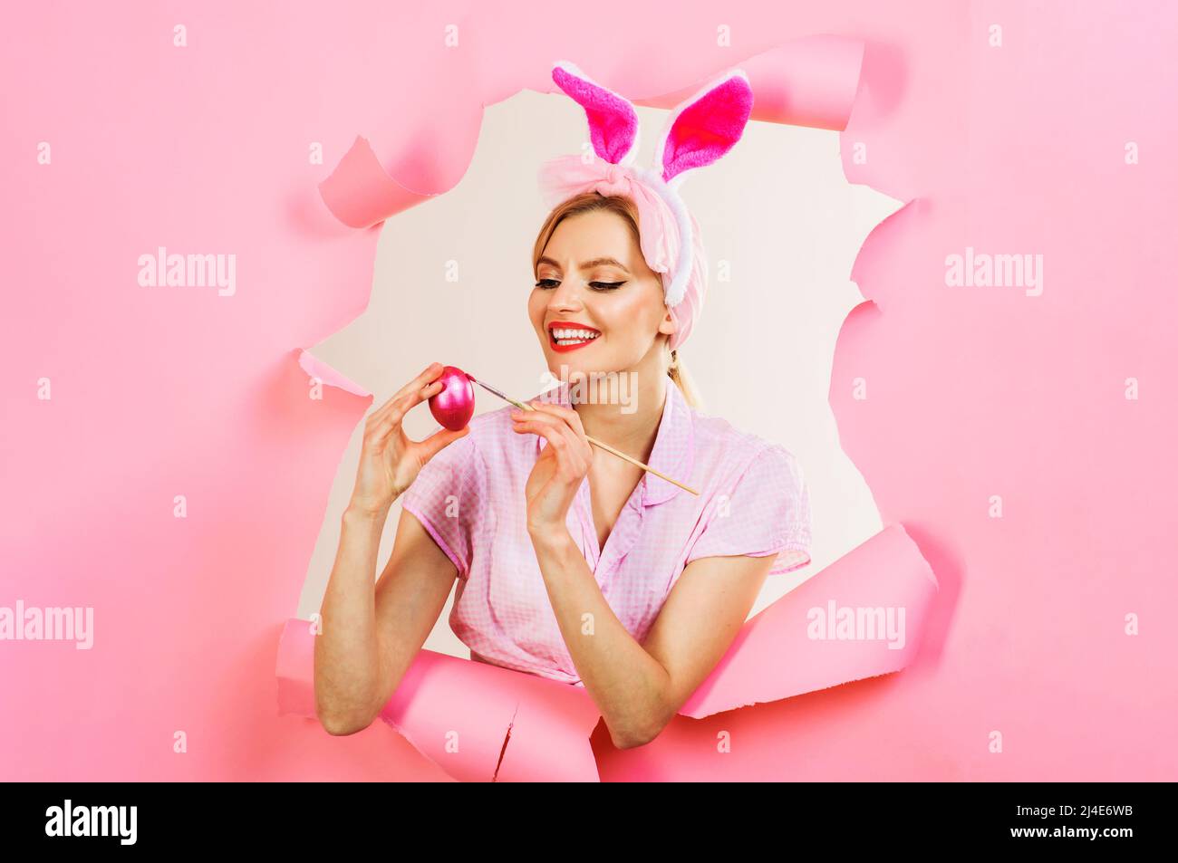 Ostern. Lächelnde Kaninchen Frau malen Ei. Hase Mädchen guckt durch Papier. Eier dekorieren Ideen. Stockfoto