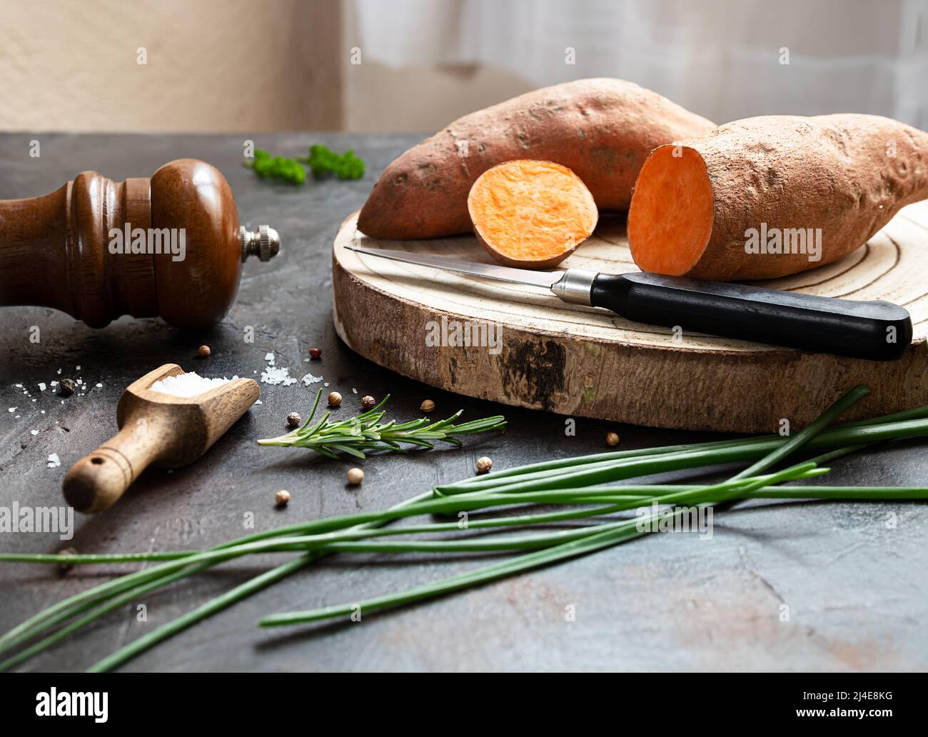 Roher Bio-Yam - Süßkartoffeln auf einem Schneidebrett und Gewürze auf einem dunklen Tisch Stockfoto