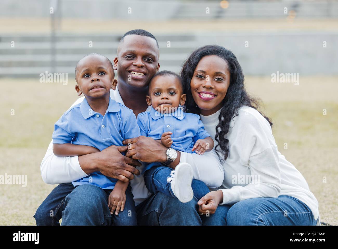 Eine wunderschöne afroamerikanische Mutter und ein wunderschöner Vater sitzen auf einer Treppe im Freien und umarmen ihre beiden Söhne und die Jungen spritzen sich Stockfoto
