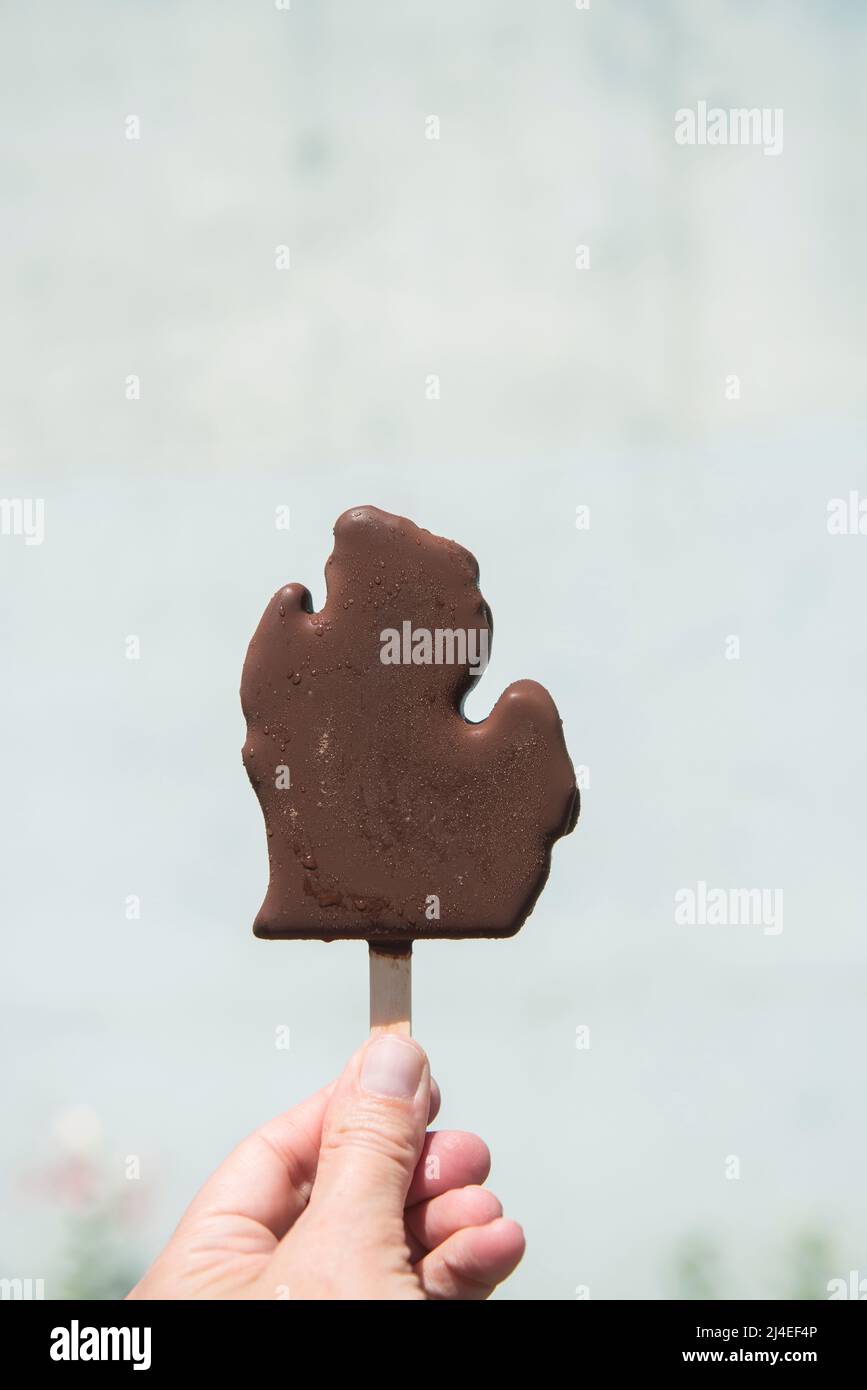 Frauenhand mit einer in Michigan-Form geformten Schokoladeneis-Bar. Minimal Michigan Foodie Frozen Treat close up Stockfoto