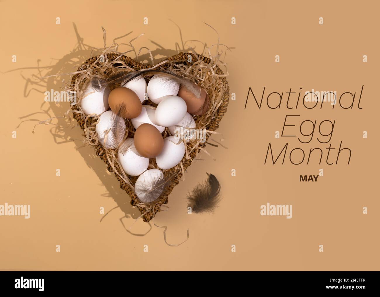 Konzept für National Egg Month. Der Name des Feiertages ist über dem Bild geschrieben. In einem herzförmigen Korb liegen weiße und braune Eier auf einem Scherben. Stockfoto