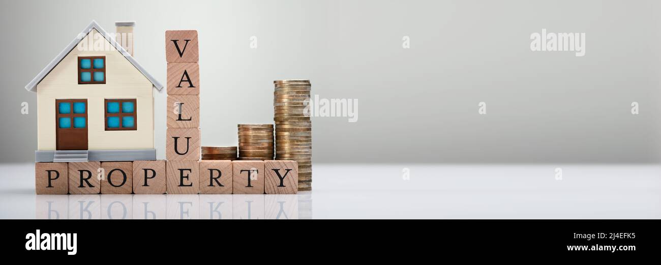 Haus Modell und gestapelte Münzen zeigen Property Value Konzept auf reflektierenden Schreibtisch Stockfoto