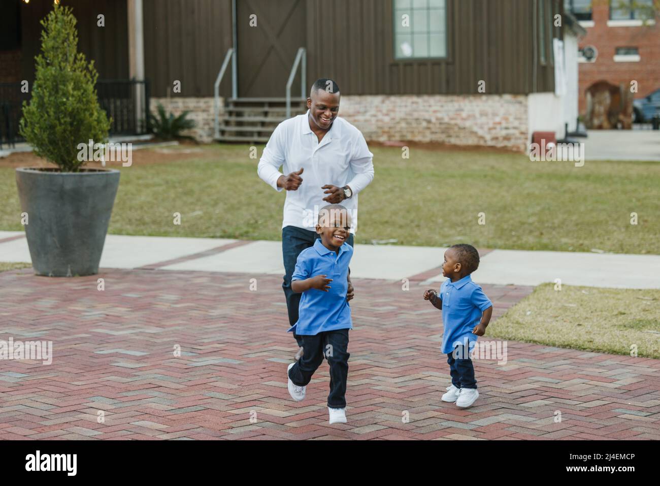 Ein Vater jagt seine beiden Söhne im Freien, während sie zusammen spielen und sich verbinden Stockfoto