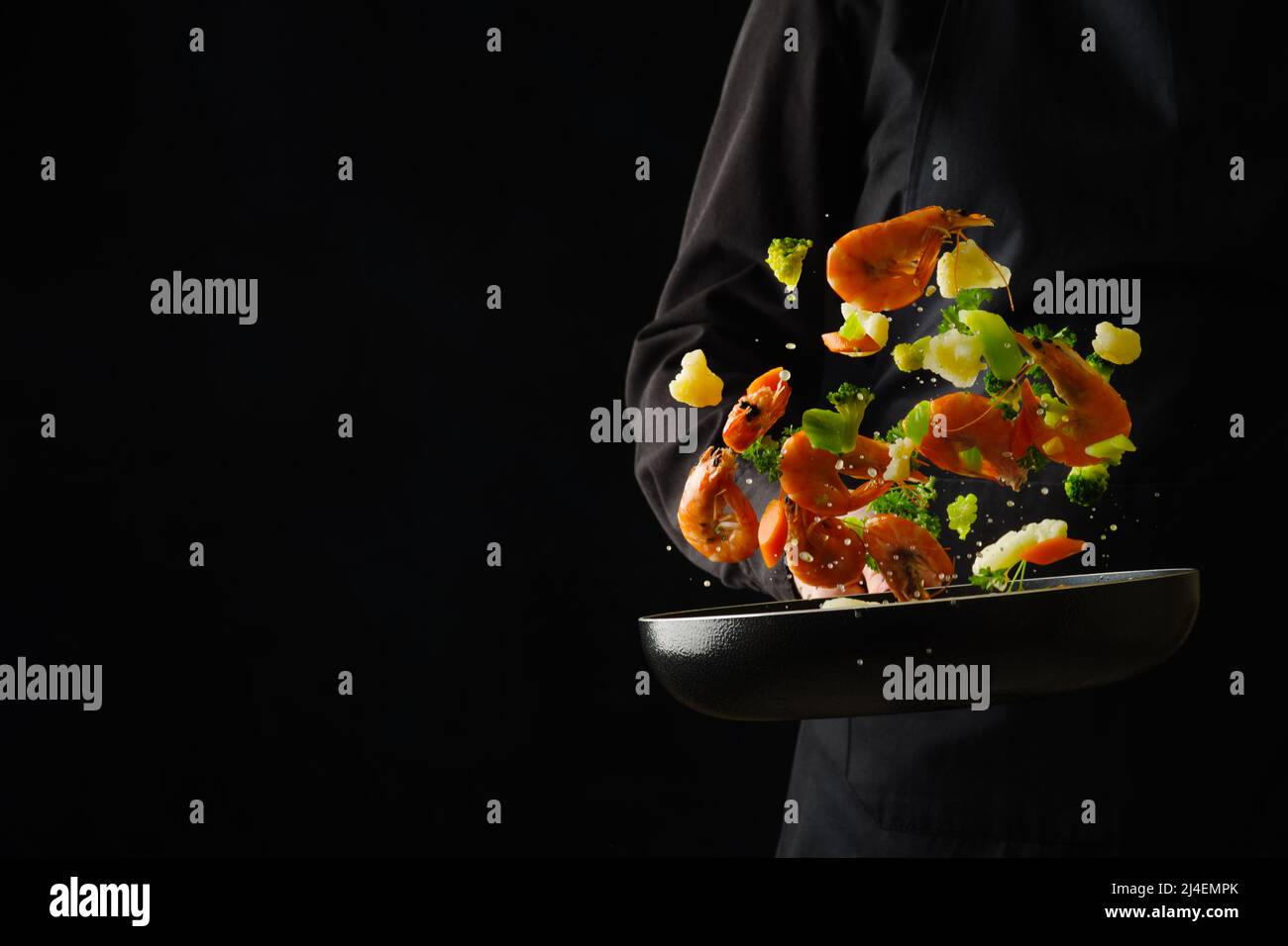 Ein professioneller Koch bereitet Meeresfrüchte mit Gemüse in einer Pfanne auf schwarzem Hintergrund zu. Gefrorenes Essen während des Fluges. Asiatische Küche, vegetarische Küche, Gou Stockfoto