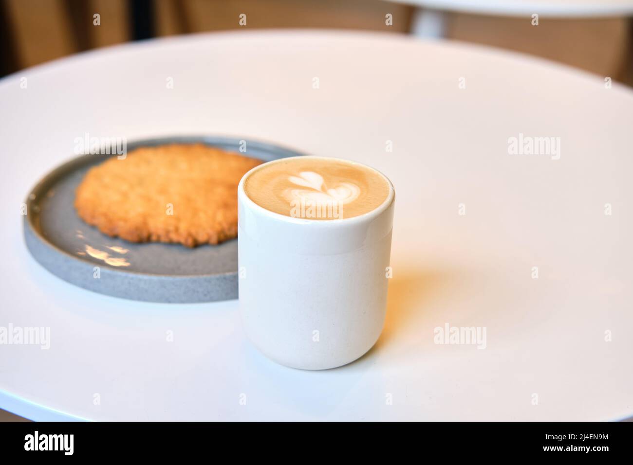 Der morgendliche Brunch im Café ist auf dem Tisch. Riesenkeks und Cappuccino mit schönem Milchschaum. Manchmal muss man in dieser schnelllebigen Welt eine Pause einlegen Stockfoto