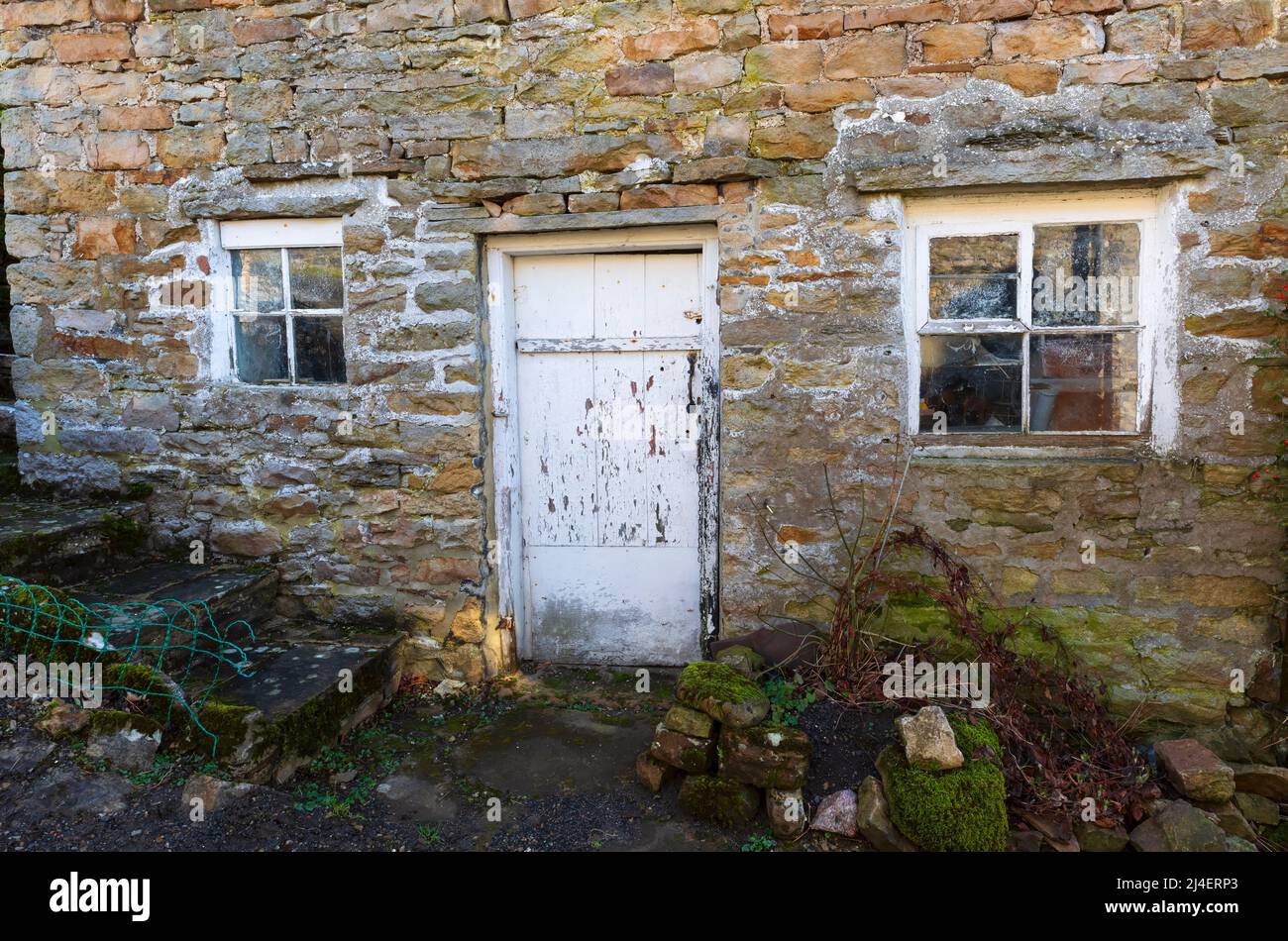 Ein altes Haus in Langthwaite, Archengarthdale, Yorkshire Dales National Park. Die Farbe blätterte von der alten Holztür und den Fenstern in einer alten Steinwand ab. Der Stockfoto