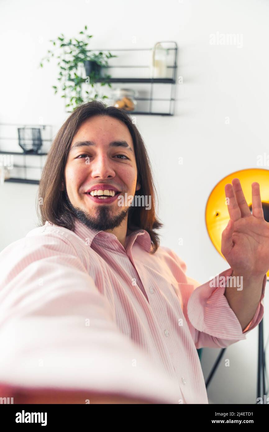 Selfie von jungen kaukasischen Mann mit langen dunklen Haaren lächelnd und winkend auf die Kamera nach Hause Hintergrund Kopie Raum . Hochwertige Fotos Stockfoto