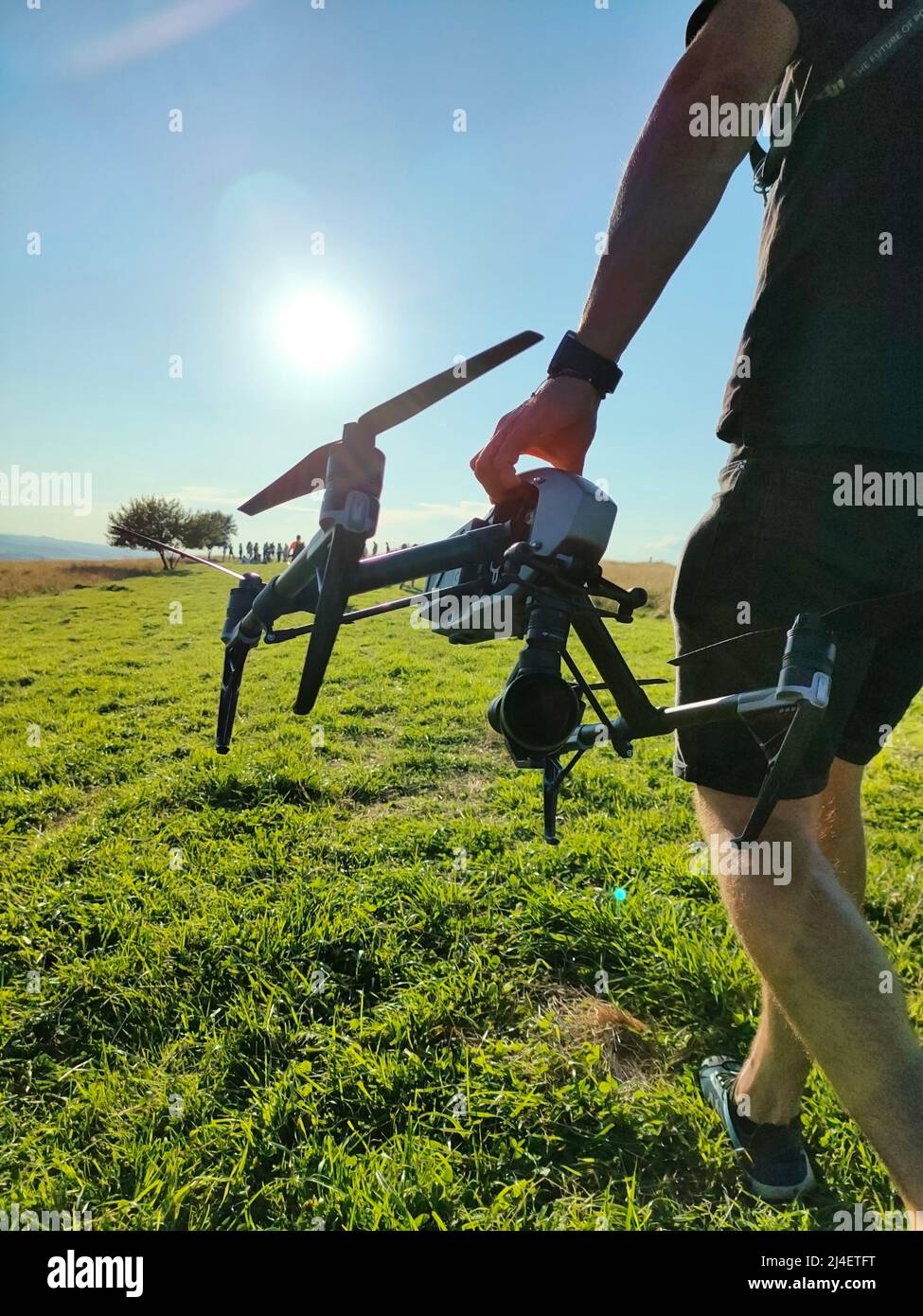 Vertikale Aufnahme eines jungen kaukasischen Schöpfers, der bei schönem Wetter die Wiese entlang läuft, während er eine Drohne hält, um aus der Luft zu Filmen. Hochwertige Fotos Stockfoto