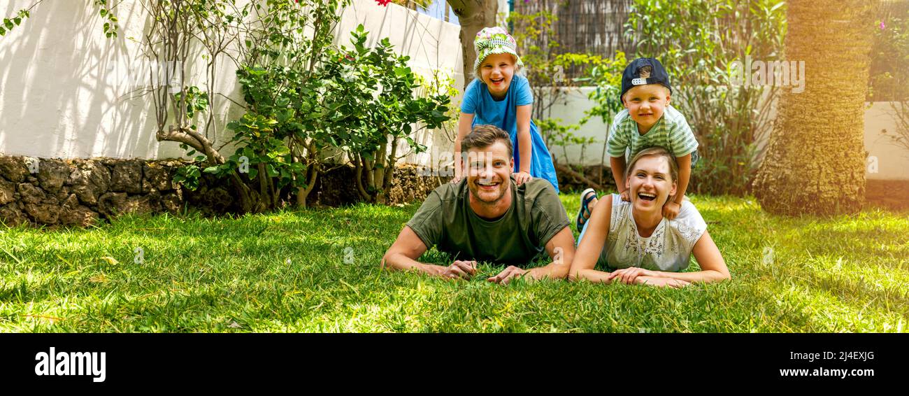 Glückliche Familie mit zwei Kindern liegen im Hause Hinterhof Garten Rasen und Blick auf die Kamera. Banner mit Kopieplatz Stockfoto