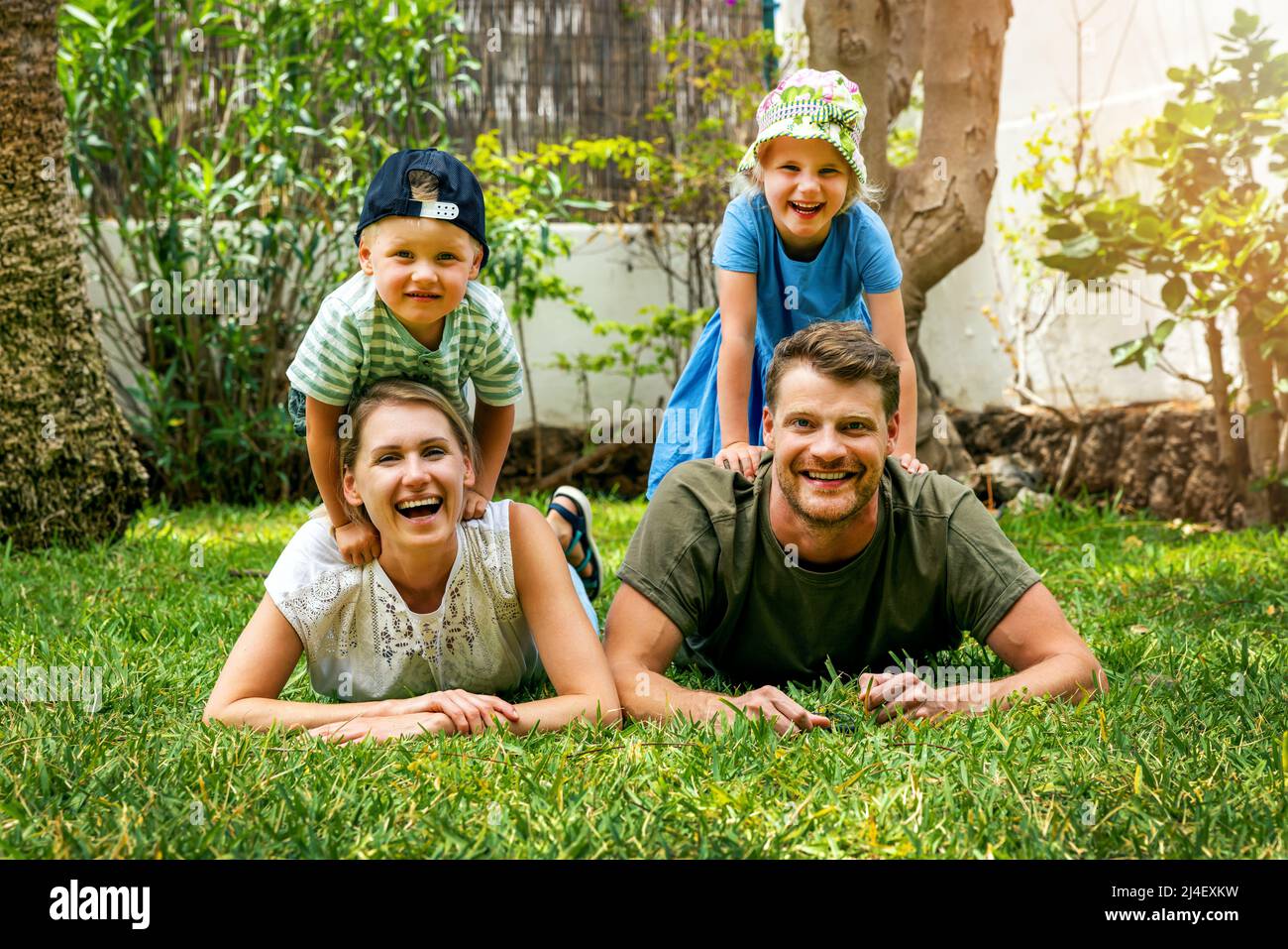 Glücklich lächelnde Familie mit zwei Kindern liegen im Hause Hinterhof Garten Gras. Blick auf die Kamera Stockfoto