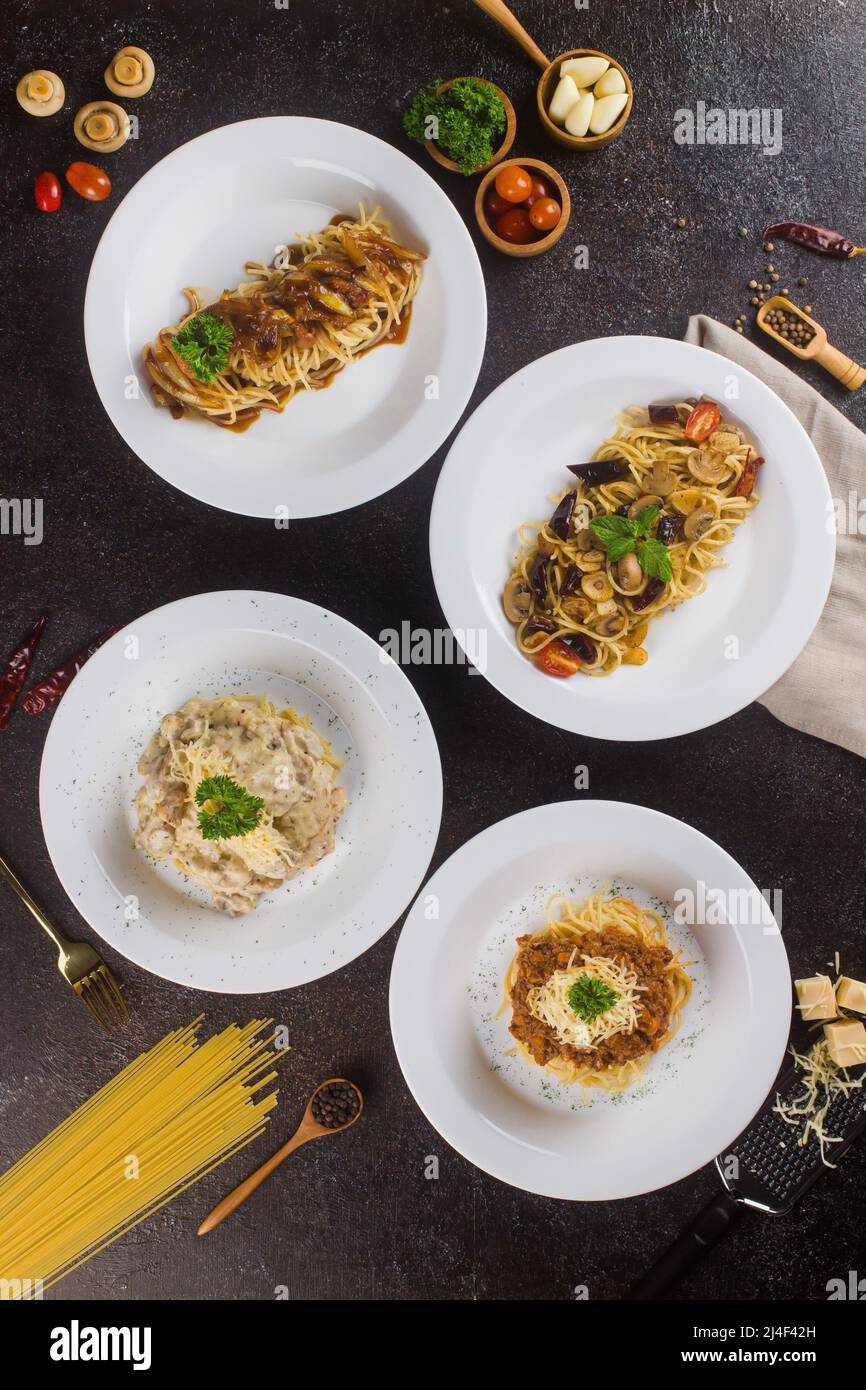 Ein Satz Pasta-Spaghetti mit Sauce, Rindfleisch, Olivenöl und frischer grüner Petersilie in einem weißen ovalen Teller mit Zutaten auf schwarzem Hintergrund Stockfoto