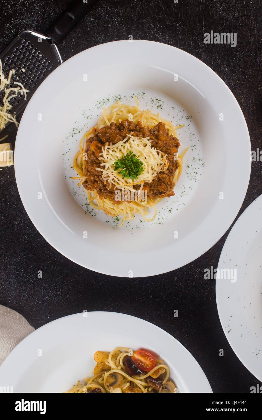 Eine gekochte Pasta-Spaghetti mit Tomatensauce, Rindfleisch, Olivenöl und frischer grüner Petersilie in einem weißen ovalen Teller mit Zutaten auf schwarzem Hintergrund Stockfoto