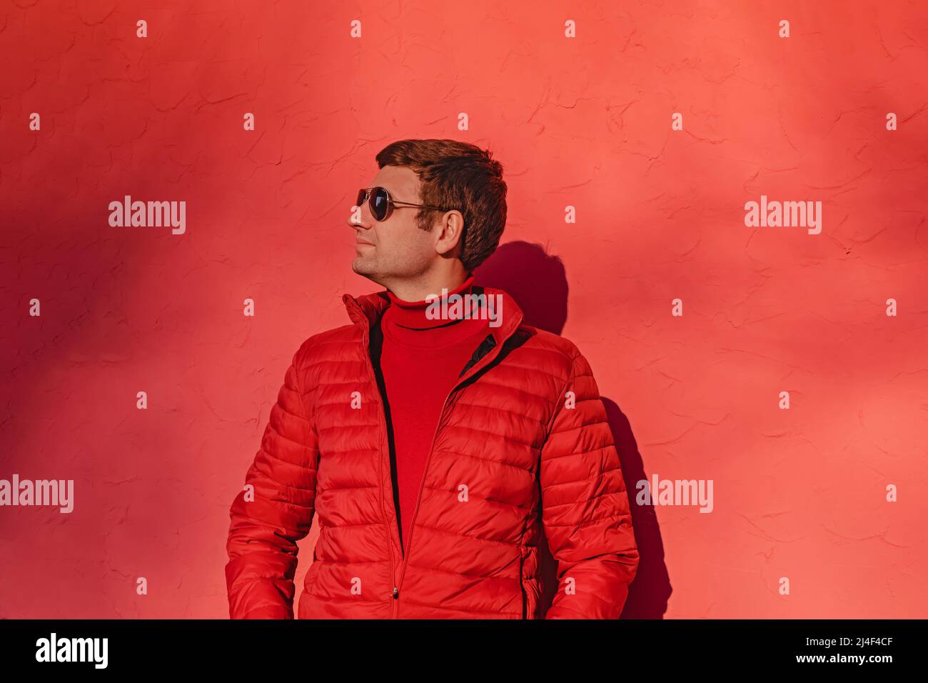 Junger Mann in rotem Pullover und Jacke in der Nähe der roten Wand  Stockfotografie - Alamy