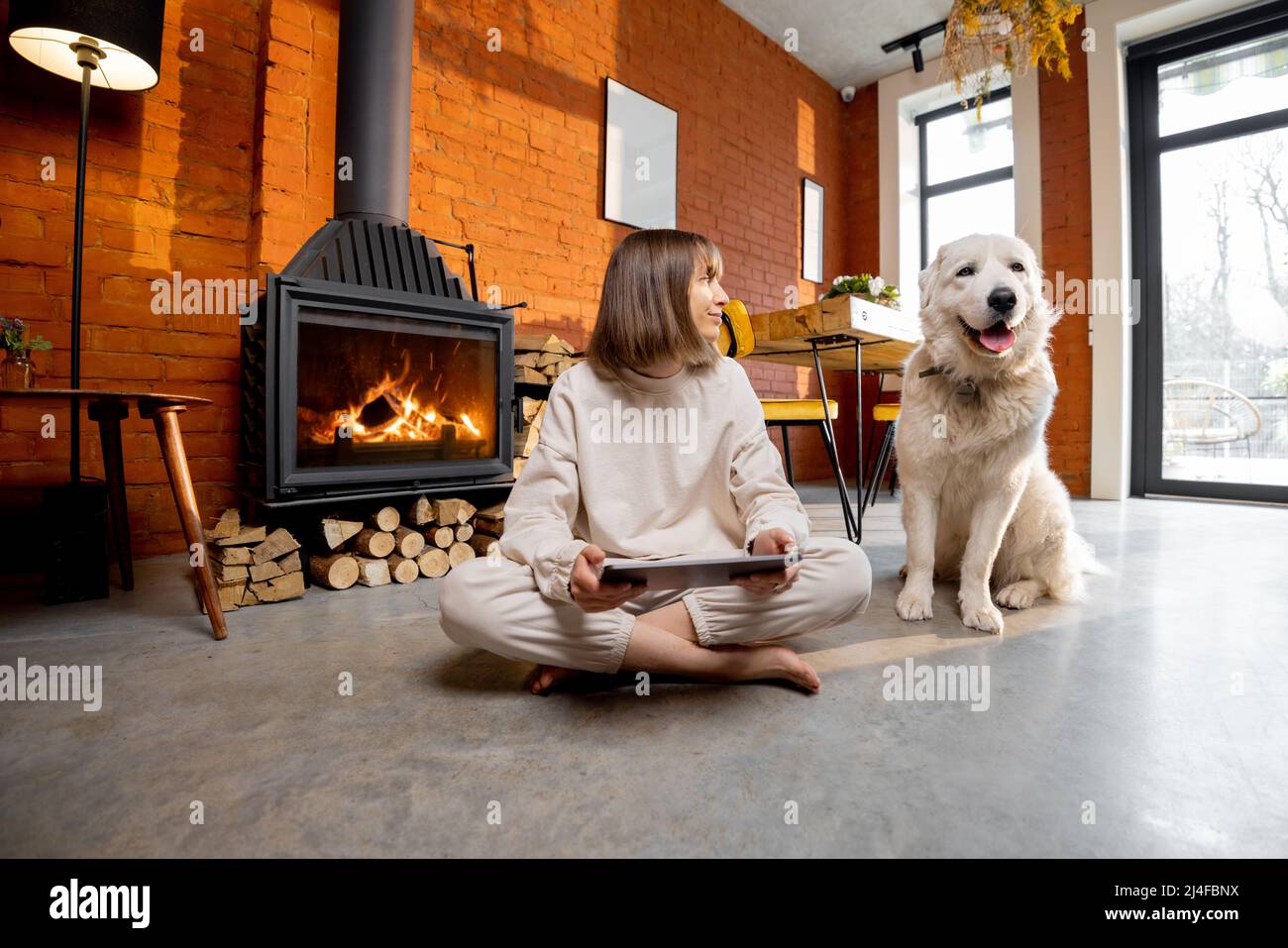 Frau saß entspannt mit ihrem Hund auf dem Boden in der Nähe des Kamins und mit digitalen Tablet zu Hause Stockfoto