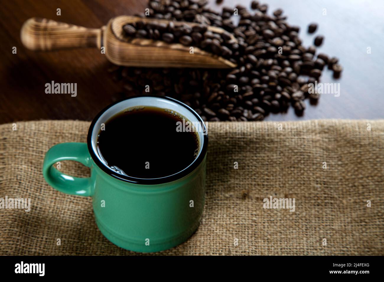 Grüne Tasse Kaffee mit Kaffeebohnen auf Holzhintergrund Stockfoto