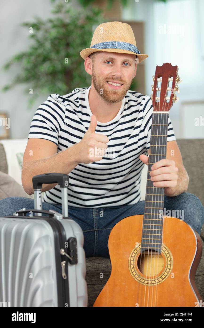 Männlicher Musiker mit Koffer und Gitarre, der die Daumen hoch hält Stockfoto