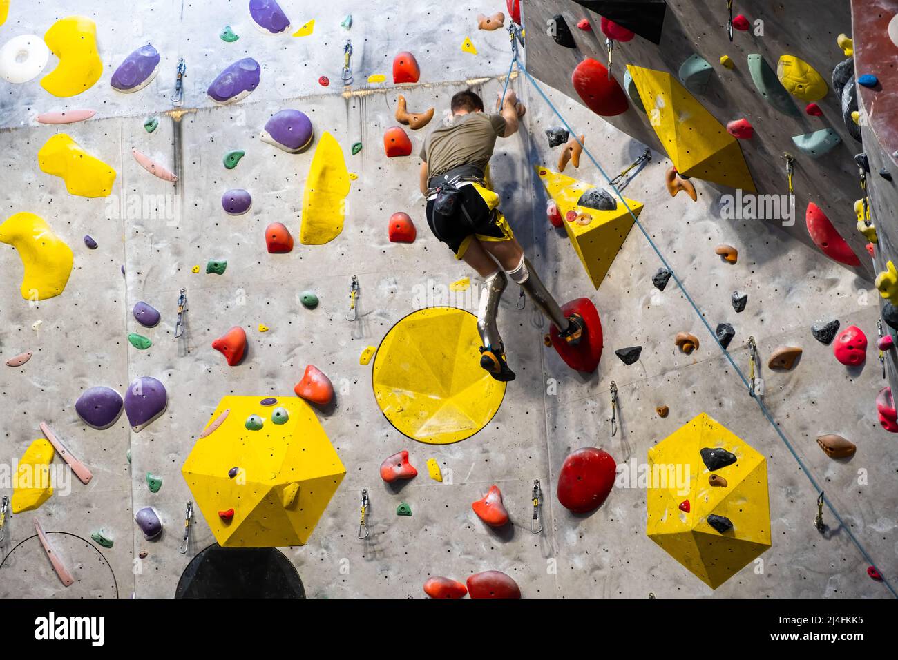 Der Kletterer trainiert an der künstlichen Felswand mit Versicherung in der Boulderhalle, April 2022, Prag, Tschechische Republik. Stockfoto