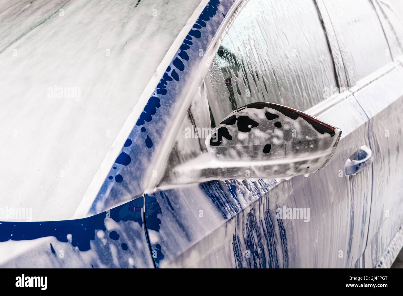 Reinigung des blauen Automobils mit Seife und Druckwasserstrahl bei der Autowaschanlage. Elektrofahrzeug in Garage gewaschen Nahansicht Stockfoto
