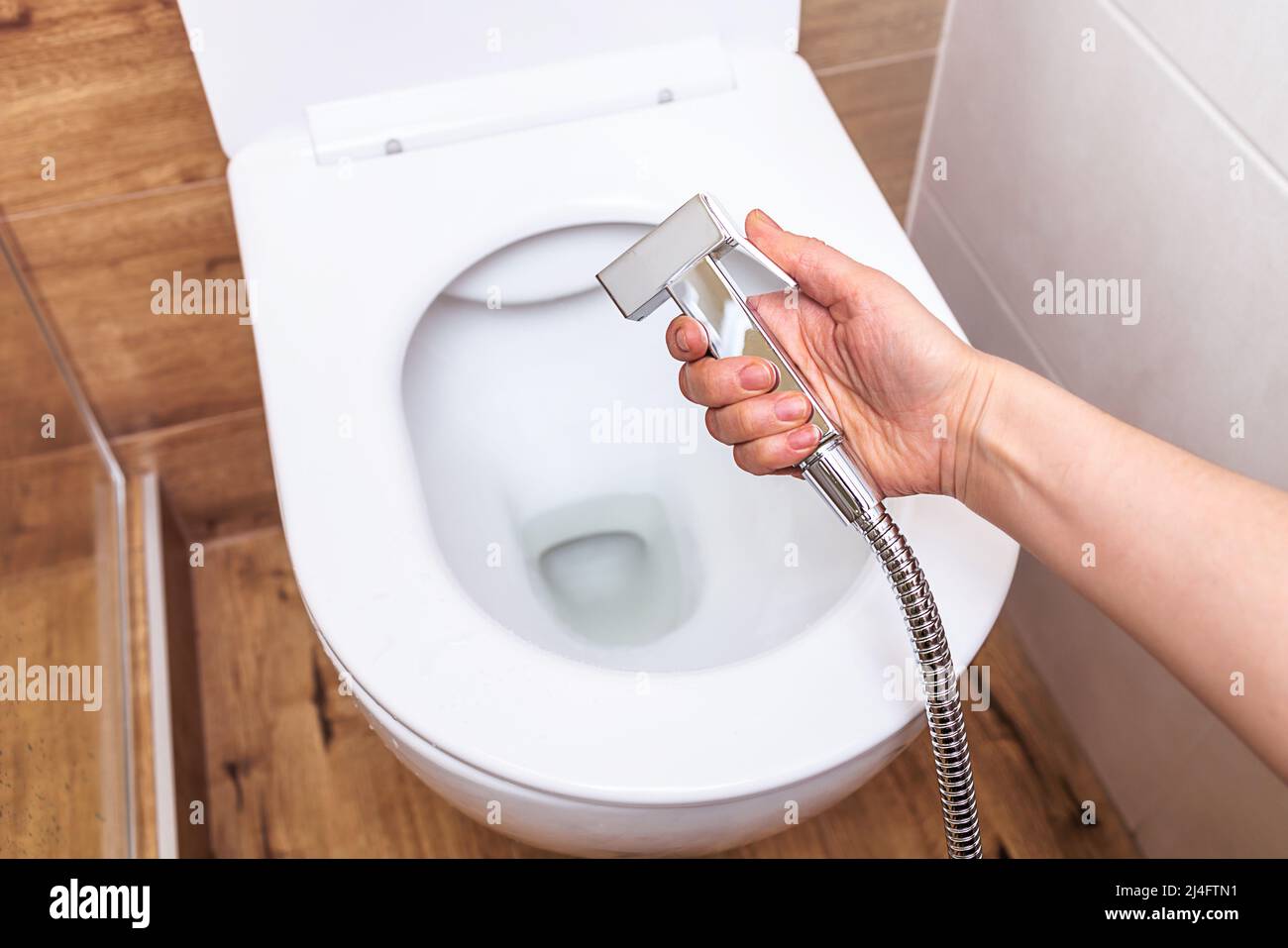 Nahaufnahme, in weiblicher Hand eine hygienische Dusche, vor dem Hintergrund einer modernen Toilette Stockfoto