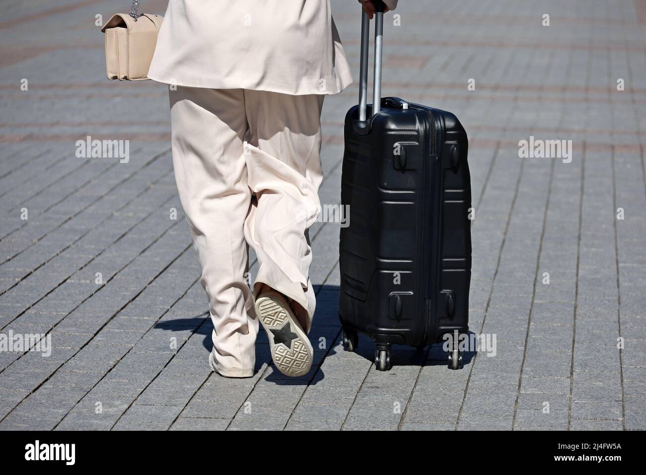 Stilvolle Frau zu Fuß mit schwarzem Koffer auf Rädern. Weibliche Beine und Gepäck auf der Stadtstraße, Reisekonzept Stockfoto