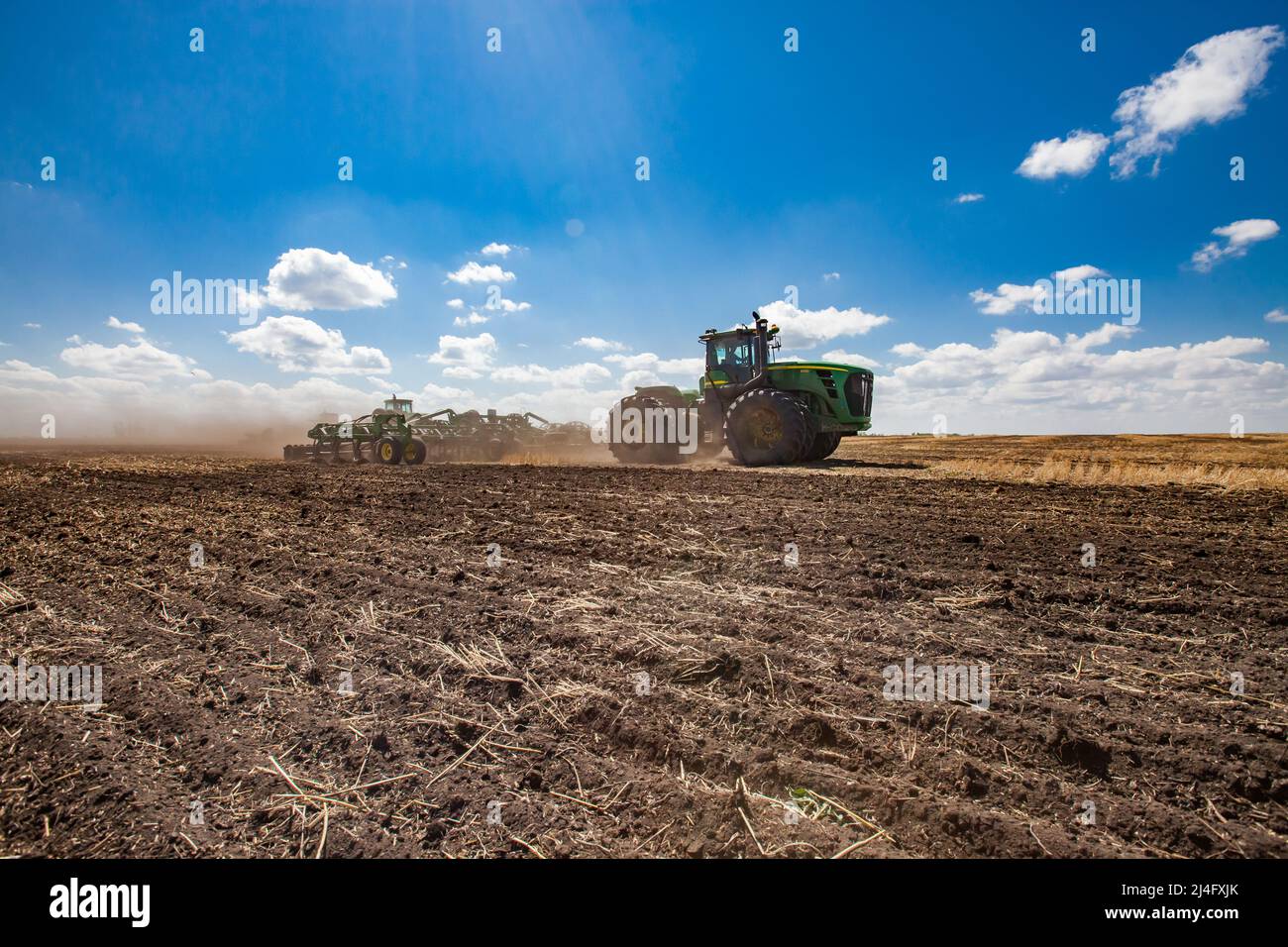Provinz Nordkasachstan, Kasachstan-12. Mai 2012: Frühjahrssaat-Kampagne. John Deere-Traktoren, die den Boden mit Egge kultivieren. Blauer Himmel, Wolken Stockfoto