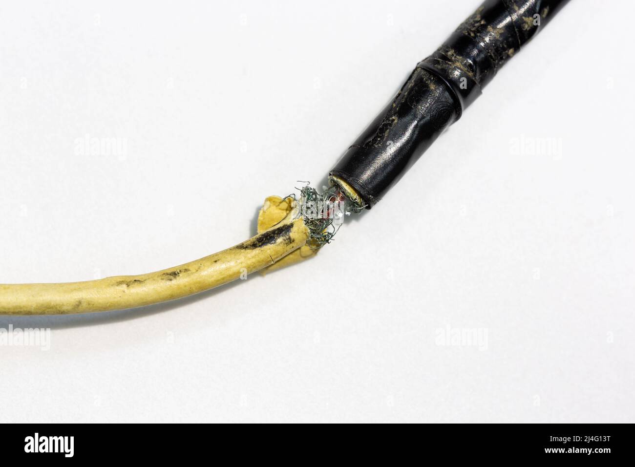 Beschädigter, beschädigter Teil des USB-Ladekabels. Die Drähte ragen aus der Außenschicht aus Kunststoff. Der usb-Anschluss des Kabels ist mit schwarzem Klebeband umwickelt. Stockfoto