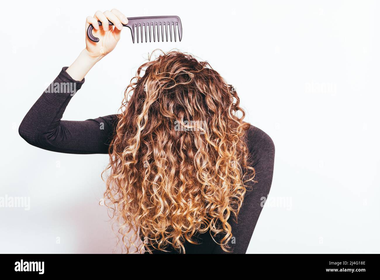 Junge Frau kämmt ihr dickes lockiges Haar mit einem breiten Kamm Stockfoto