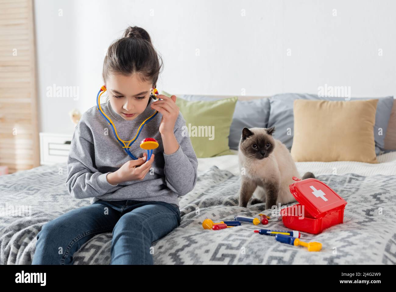 Mädchen mit Spielzeug Stethoskop spielen Arzt auf dem Bett in der Nähe von Katze und erste-Hilfe-Kit Stockfoto