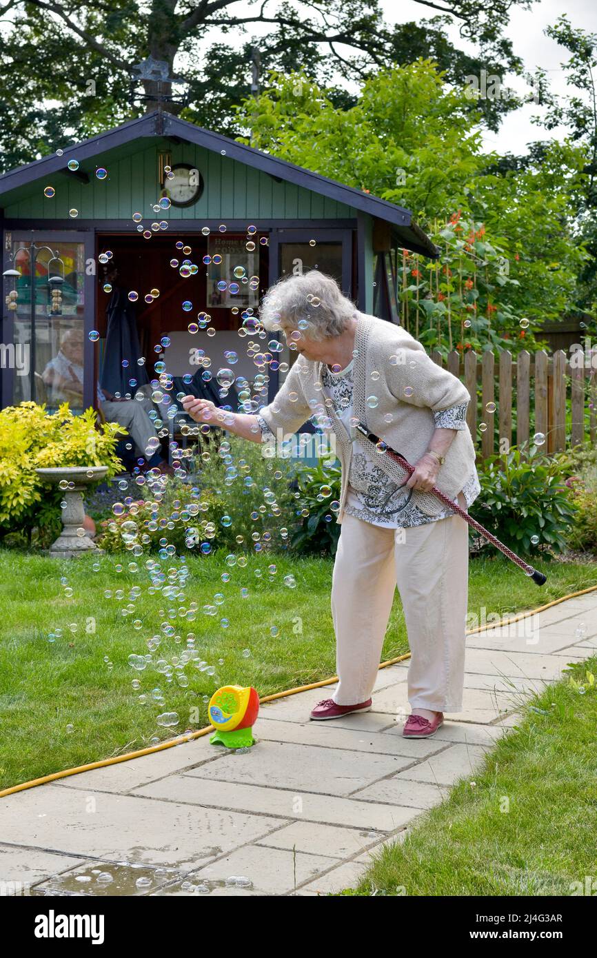 Großmutter, die Spaß mit Blasen im Garten hat und beweist, dass du nie zu alt bist, um ein Kind zu sein! Konzept der jungen Menschen im Herzen. Stockfoto