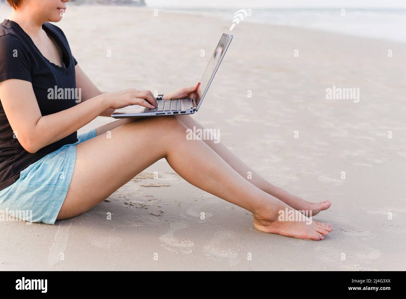 Lifestyle-Frau Freiberuflerin, die am Strand an einem Laptop arbeitet. Stockfoto