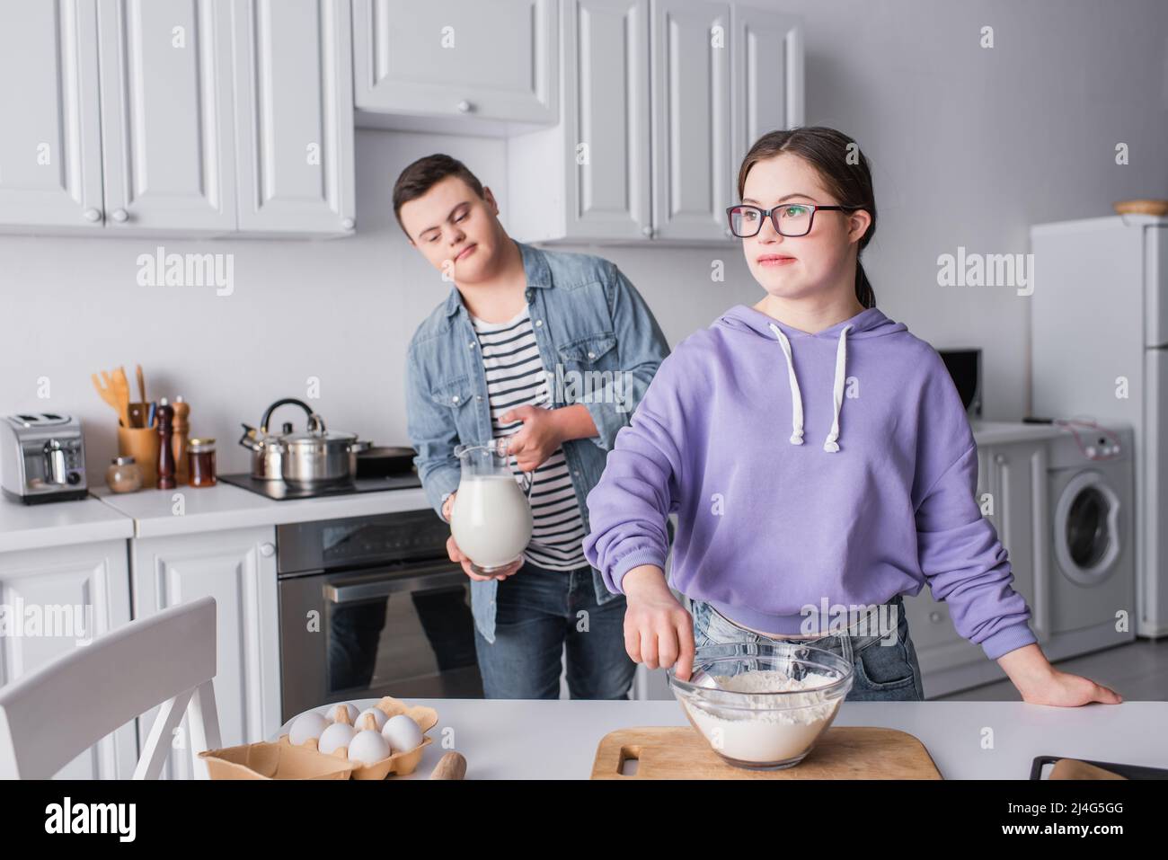 Teen Mädchen mit Down-Syndrom Kochen in der Nähe Freund mit Milch in der Küche Stockfoto