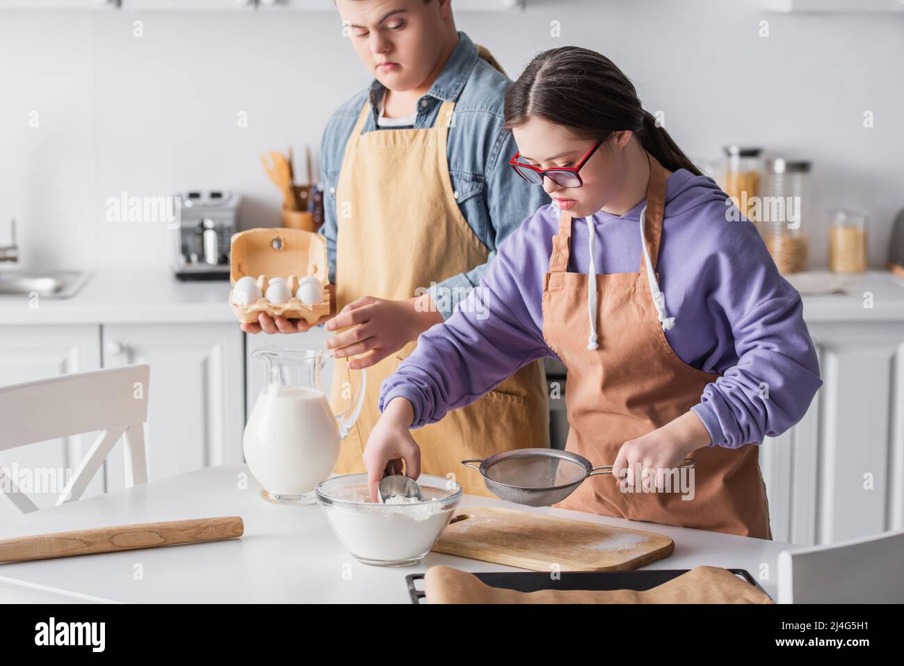 Mädchen mit Down-Syndrom Kochen in der Nähe Freund hält Eier in der Küche Stockfoto