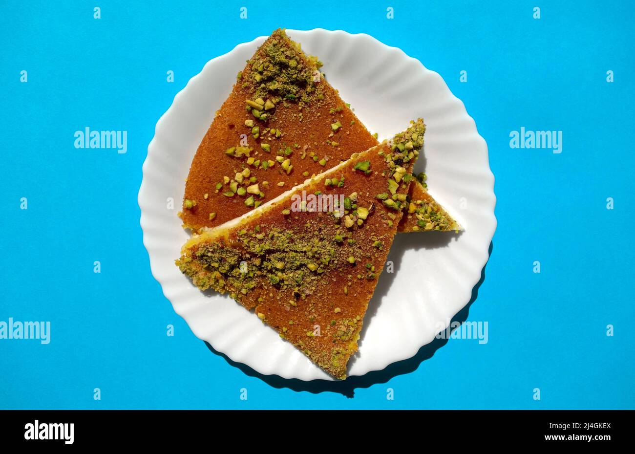 Traditionelles östliches Dessert Kunafa. Draufsicht auf arabischen Käse Kunafa in weißer Platte auf hellblauem Hintergrund. Konafa Stockfoto